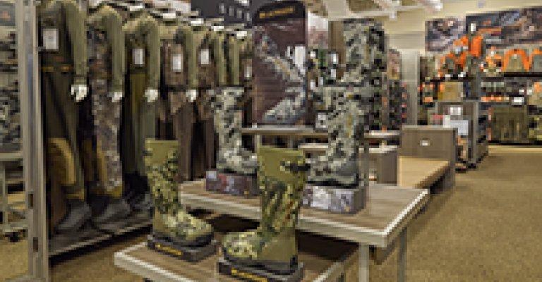 An end isle of some camo bibs and other hunting clothing, and a display of hunting boots and other hunting shoes.